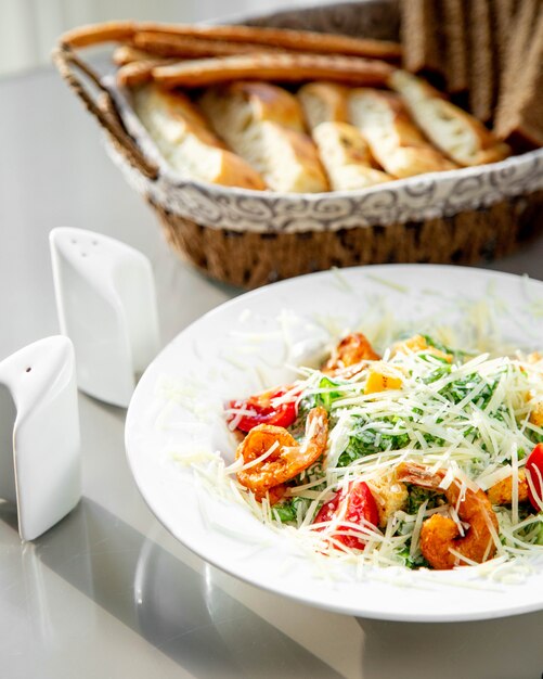 A plate of shrimp caesar salad served with bread basket, salt and pepper