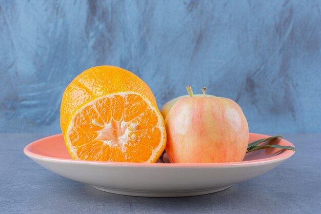 Тарелка вкусных яблок и апельсинов на темной поверхности