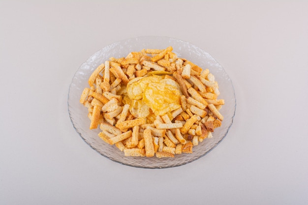 Plate of tasty crispy crackers and chips on white background. High quality photo