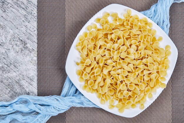 A plate of uncooked pasta with blue tablecloth on marble table.