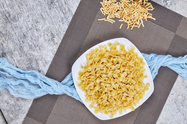 A plate of uncooked pasta with blue tablecloth on marble table.