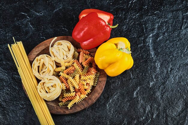 Plate of uncooked various pasta and peppers on dark table.