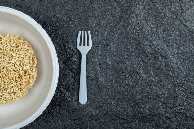 Plate of unprepared noodles on a dark background. 