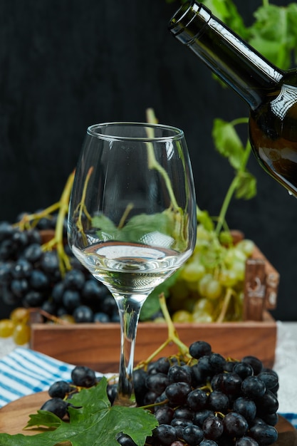 A plate of variety of grapes with a glass of white wine on white table with wine bottle