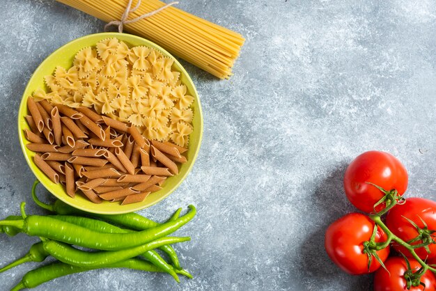 大理石の背景にさまざまなパスタ、唐辛子、トマトのプレート。