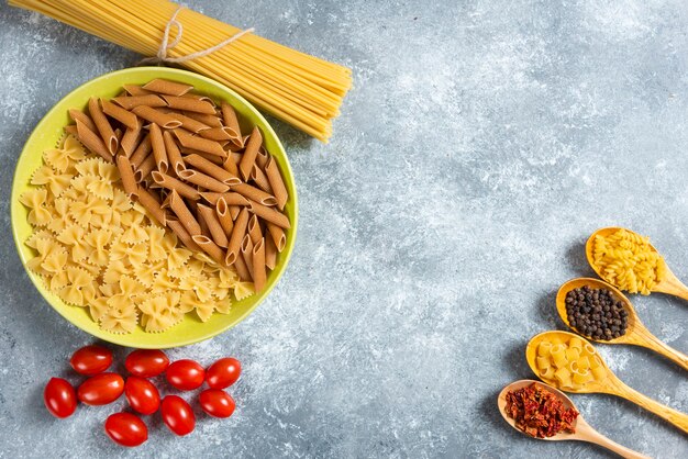 Plate of various pasta, spaghetti and tomatoes on marble background.