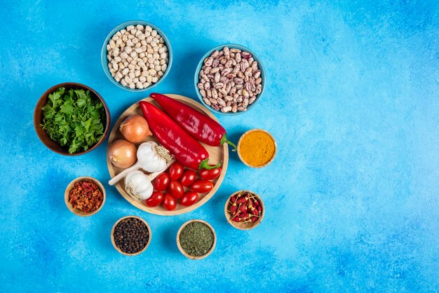 Plate of vegetables, beans and spices on blue background.