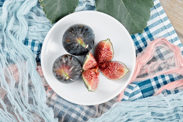 A plate of whole and sliced black figs, a leaf and blue and pink tablecloths on wooden table.