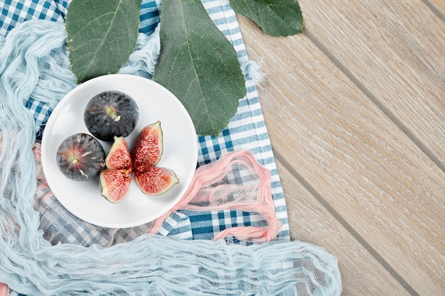 A plate of whole and sliced black figs, a leaf and blue and pink tablecloths on wooden table.