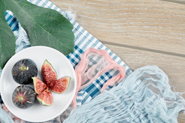 A plate of whole and sliced black figs with blue and pink tablecloths on wooden table.