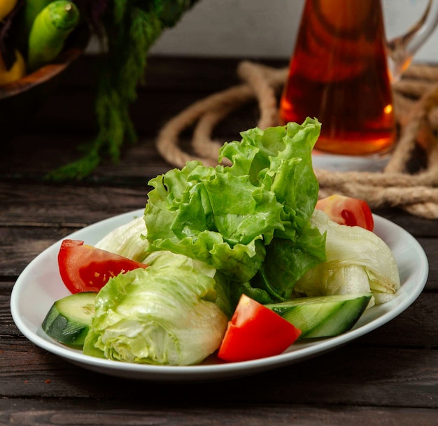 Тарелка с нарезанным помидором и огурцом и листьями салата на столе