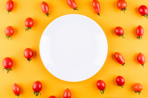 тарелка с копией пространства в окружении красных свежих помидоров черри на желтом