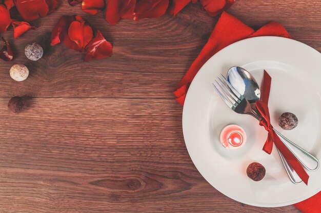 Plate with cutlery rolled into a red bow and rose petals