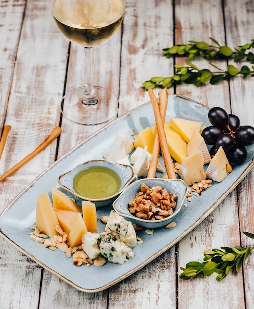 Foto gratuita piastra con diversi formaggi e uva e bicchiere di vino bianco