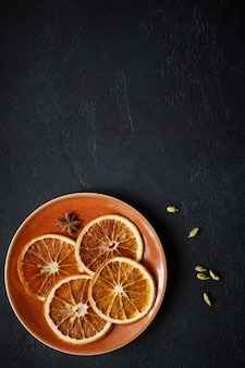 복사 공간이 있는 검정 슬레이트 배경에 바드잔과 카다멈이 있는 말린 오렌지 조각이 있는 접시
