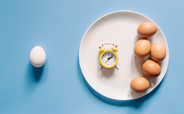 Plate with eggs and an alarm clock on a blue background flat lay