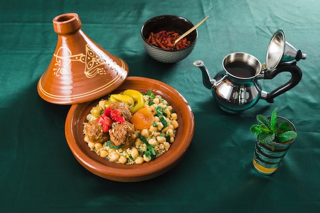 Plate with food near dry fruits, cup of drink and teapot