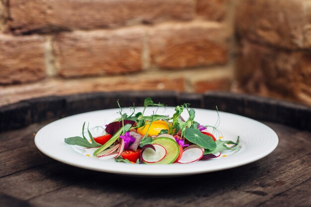 Plate with fresh salad on wooden barrel