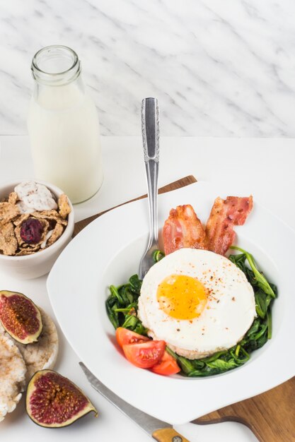 Plate with fried egg with spinach; bacon and tomatoes on white background