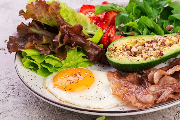 Plate with a keto diet food. Fried egg, bacon, avocado, arugula and strawberries. Keto breakfast.