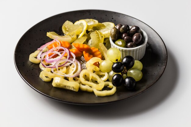 Plate with marinated pickles, pepper, onions and carrots with white and black grapes and olives