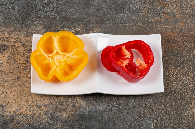 Plate with yellow peppers on the right and red peppers on the left  on the marble surface