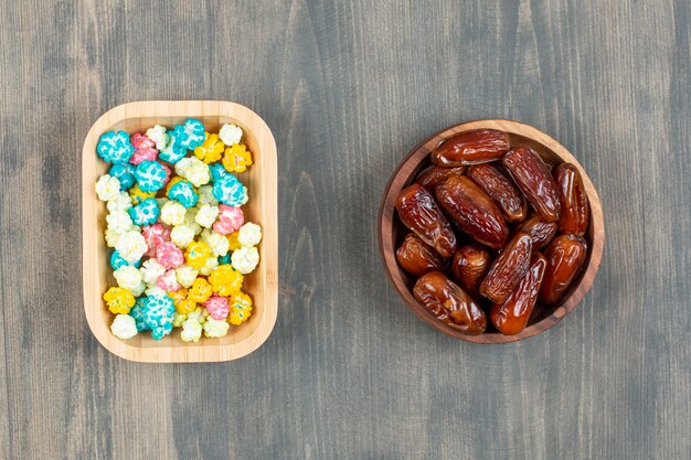 Plates of dates and colorful popcorns on wooden surface