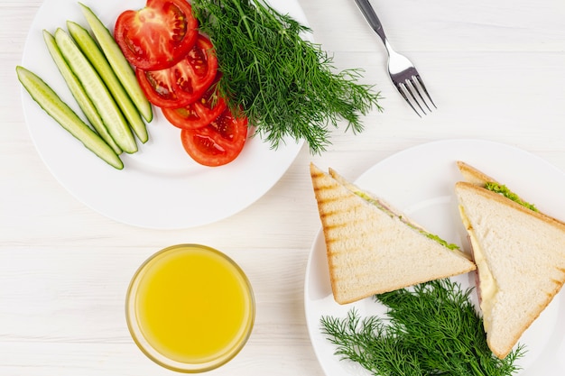 Plates with vegetables and sandwiches on a white table