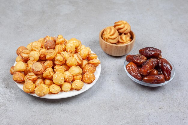 Platter and bowl full of cookie chips and a small pile of dates on marble background. High quality photo