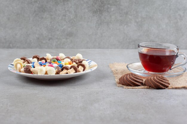 대리석 배경에 차와 쿠키 한잔 옆에 사탕과 초콜릿 버섯의 플래터. 고품질 사진