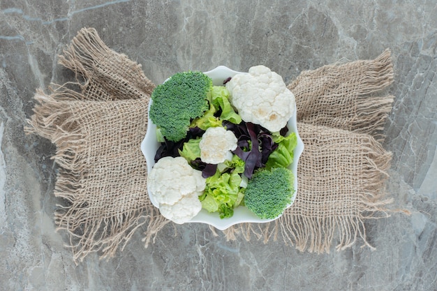 Platter of cauliflower and broccoli on a cloth wrapped pedestal on marble.