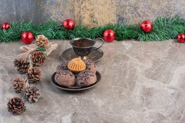 Platter of cookies, cup of tea, bundle of pine cones and a wreath on marble.