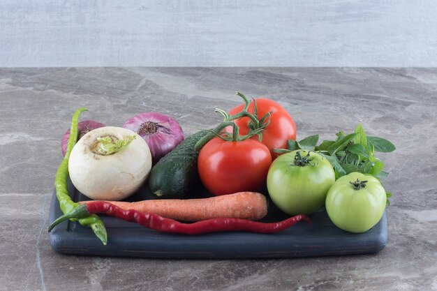 Platter of cucumber, carrot, red and green tomatoes, white turnip, green and red peppers, red onions and mint on marble surface