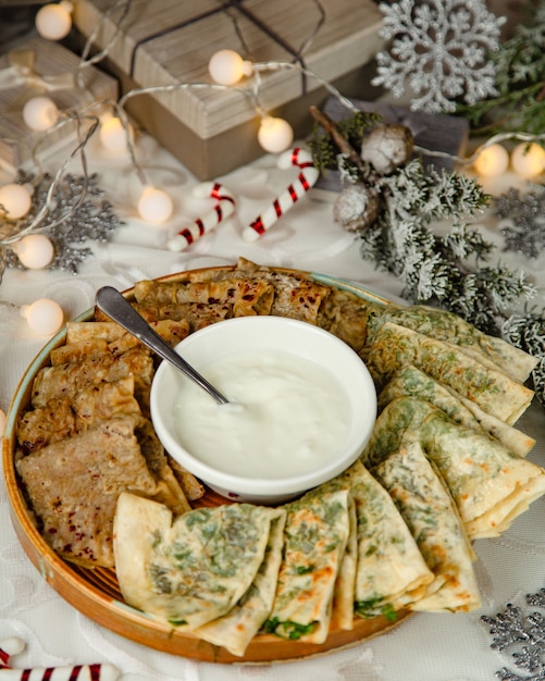 Platter of gutab stuffed flatbreads with herbs and meat fillings served with yogurt