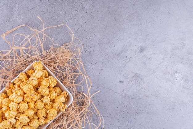 Platter on a pile of straw filled with a heap of popcorn candy on marble background. High quality photo