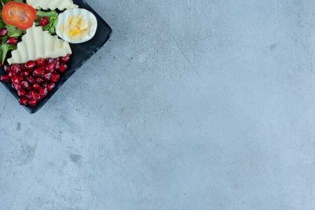 Platter of pomegranate arils, cheese, egg and pepper slices on marble surface