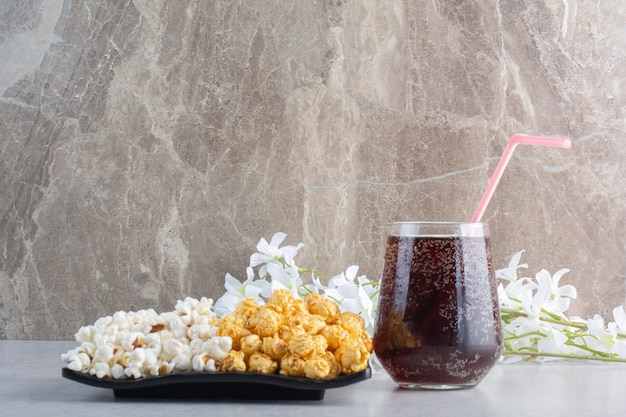 A platter of popcorn, a glass of cola and a bunch of flowers on marble.