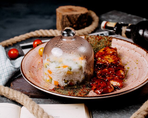 A platter of rice dish with vegetables served under the glass cover with chicken pieces and herbs