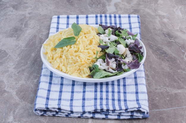 Free photo platter of rice pilau accompanied by a salad mix of amaranth, basil and cauliflower on folded towel on marble surface