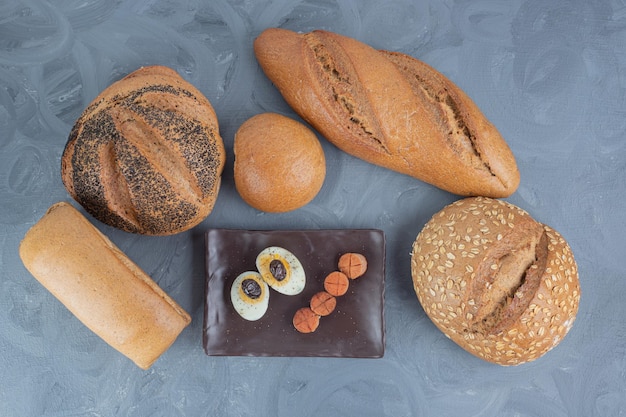 Platter of sausage and egg slices next to loaves of bread on marble table.