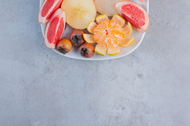 A platter of sliced grapefruits, pears and a peeled tangerine on marble background. 