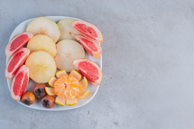 A platter of sliced grapefruits, pears and a peeled tangerine on marble background. 