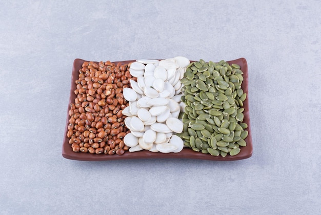 Platter stocked with red kidney beans, white pumpkin seeds and pepitas on marble surface