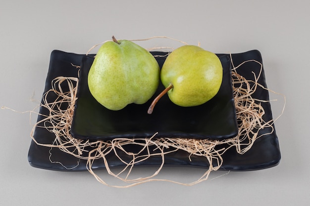 A platter with pears on a platter with straw on marble 