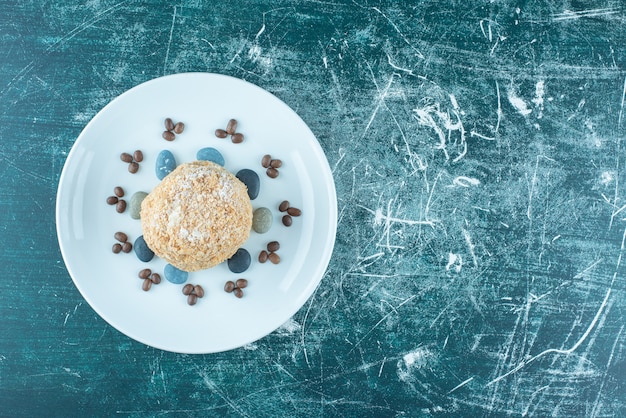 Un piatto con torta di scoiattolo, rocce di caramelle e chicchi di caffè sul blu.