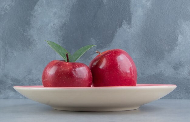 A platter with two apples on marble . 