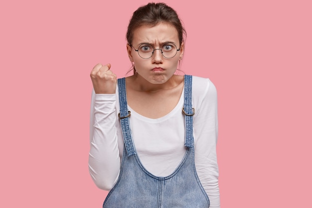 Free photo do not play with me. outraged angry teenager raises fist, frowns face, feels annoyed, has pissed expression, demonstrates threaten gesture