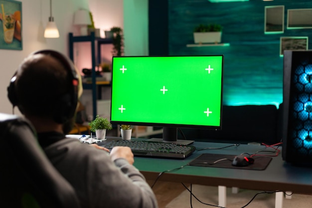 수평 녹색 화면으로 컴퓨터를 보고 있는 플레이어. 모니터에서 비디오 게임을 하기 위해 크로마 키가 있는 격리된 템플릿과 모형 배경을 사용하는 남자. 게이머 지주 컨트롤러입니다.