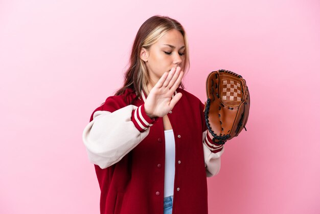 ピンクの背景に分離された野球グローブを持つプレーヤーロシアの女性は、停止ジェスチャーを作成し、失望した