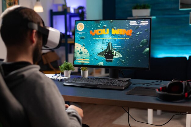 Игрок, использующий очки vr, чтобы выиграть видеоигры на компьютере. Человек с контроллером и гарнитурой виртуальной реальности играет в игру, чтобы повеселиться с современной деятельностью. Геймер, выигравший онлайн-соревнование